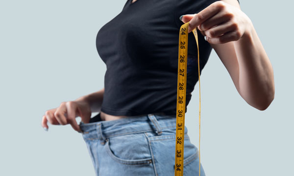 Woman holding loose pants and measuring tape